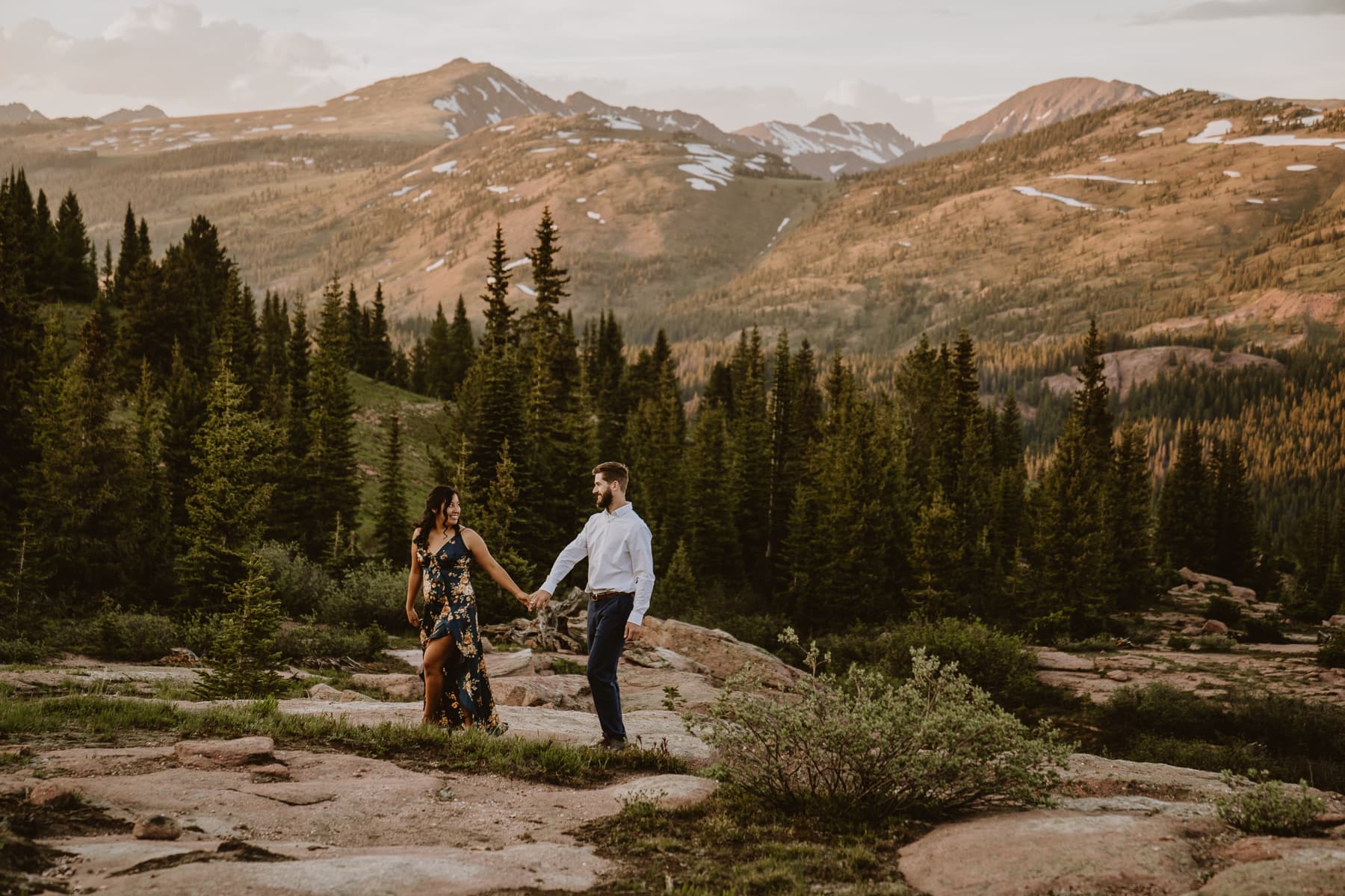 Couple walks along the rocks with towering Colorado mountains behind them. Talk about the best place to elope in Colorado!