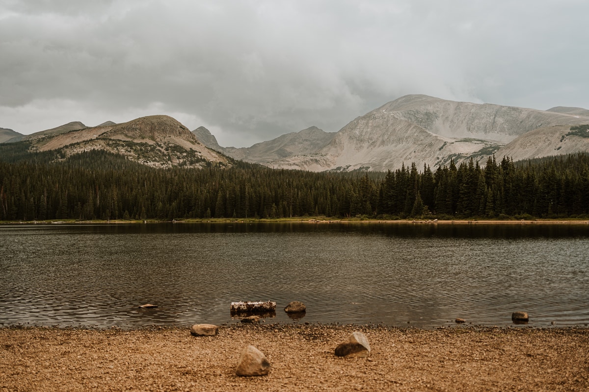 Photo of Brainard Lake from the southern shore of the lake. The skies are dark as a rainstorm hangs over the mountains.
