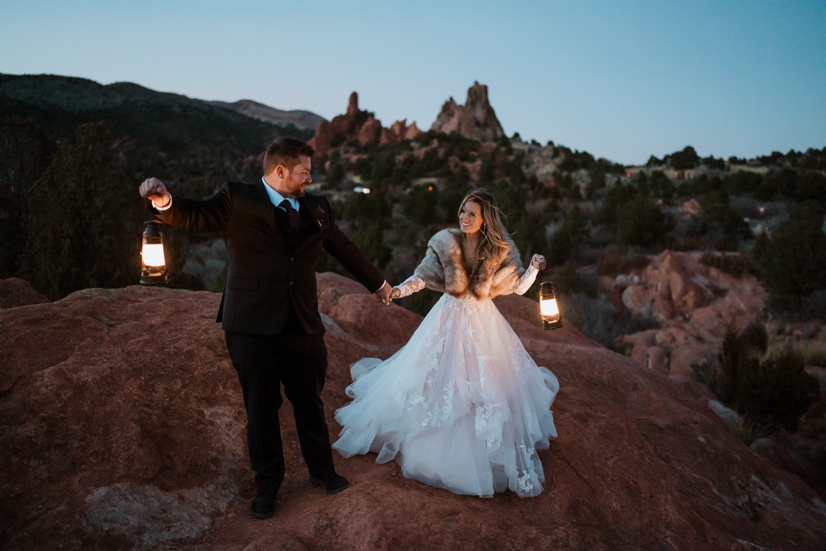 Bride and groom walk and in hand at High Point Overlook for their sunset elopement. Central Garden shines behind them, and lanterns light up their faces just enough to see their smiles.
