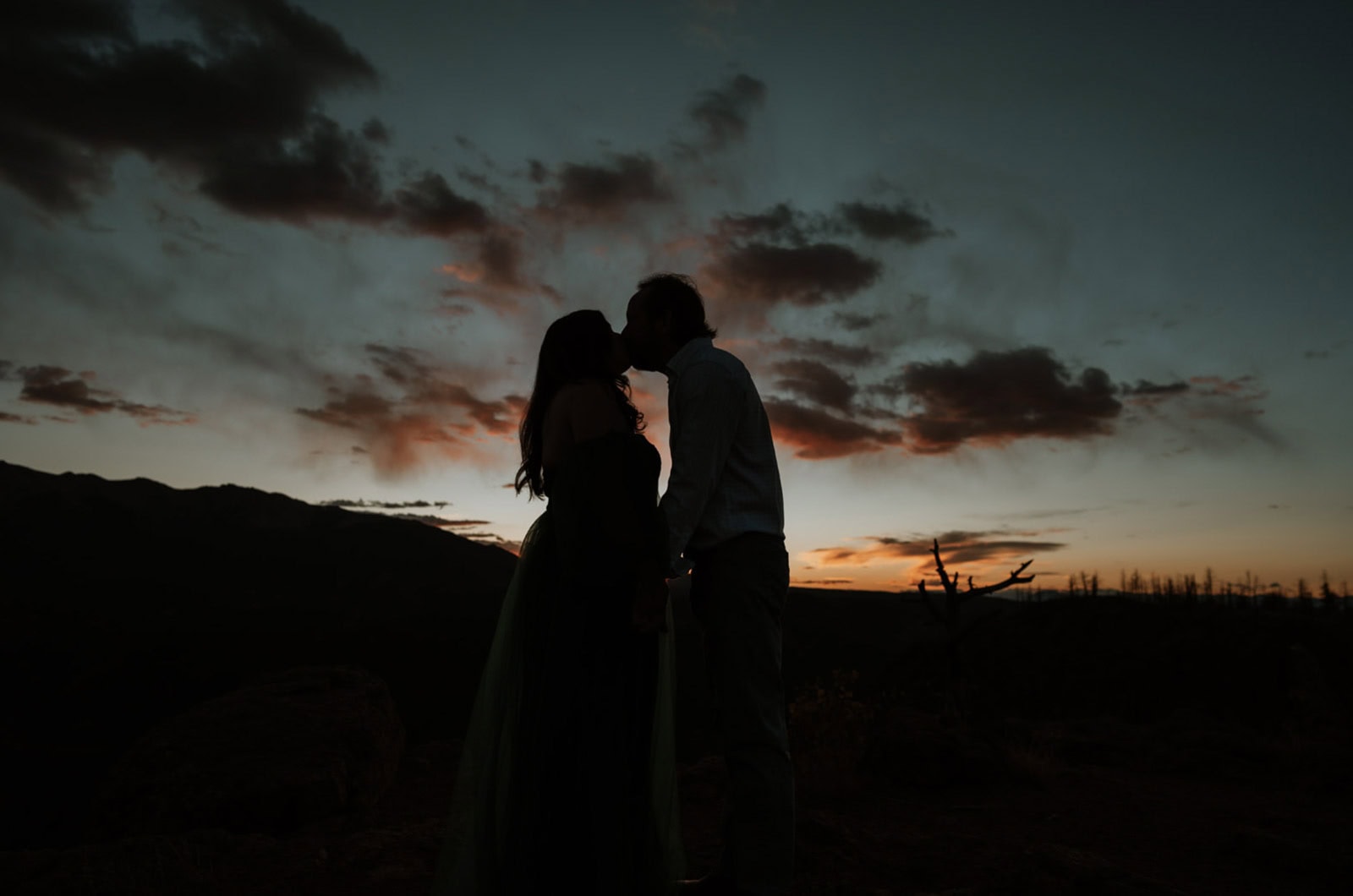 A silhouette kiss under a painted sunset sky, with dramatic clouds and fading light setting the tone for this garden of the gods elopement portrait.