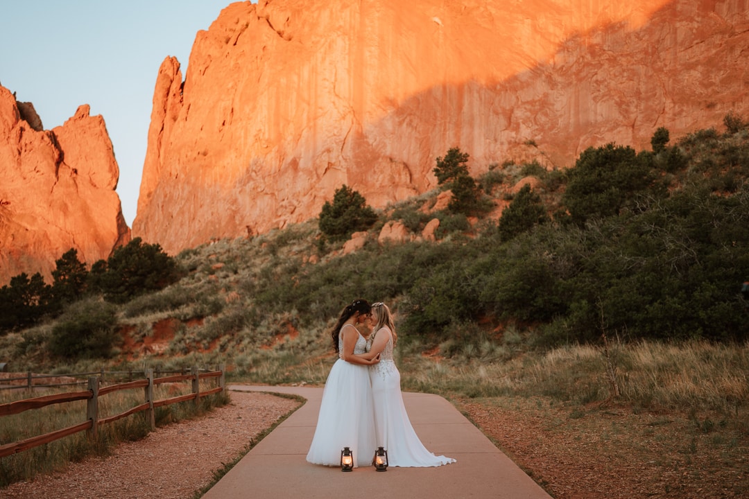 Two brides hold each other in front of a giant rock structure in the middle of Central Garden at sunrise. These formations are why the couple chose to have their elopement in Garden of the Gods.