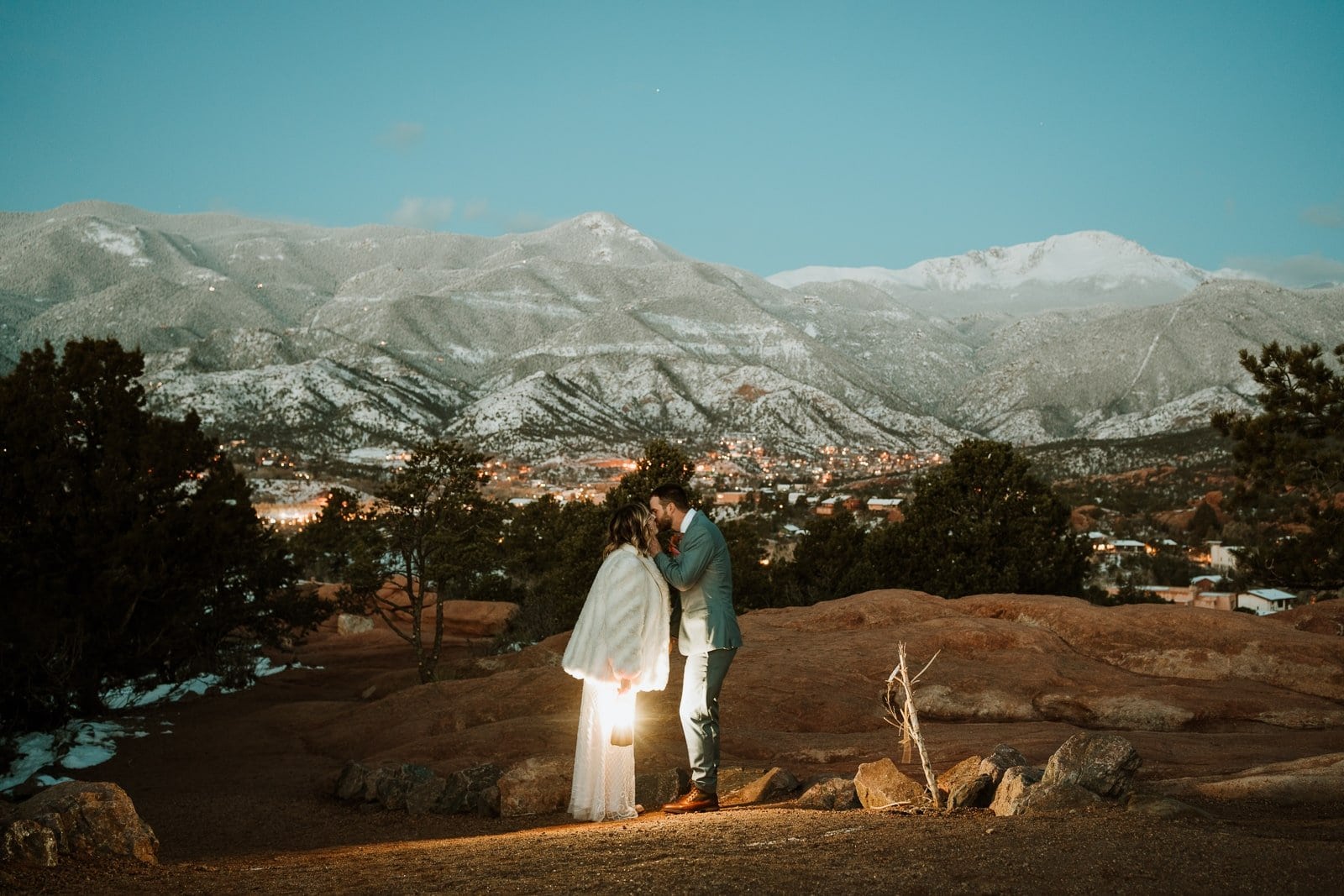A bride and groom holding a lantern share a kiss just before their sunrise Garden of the Gods elopement.