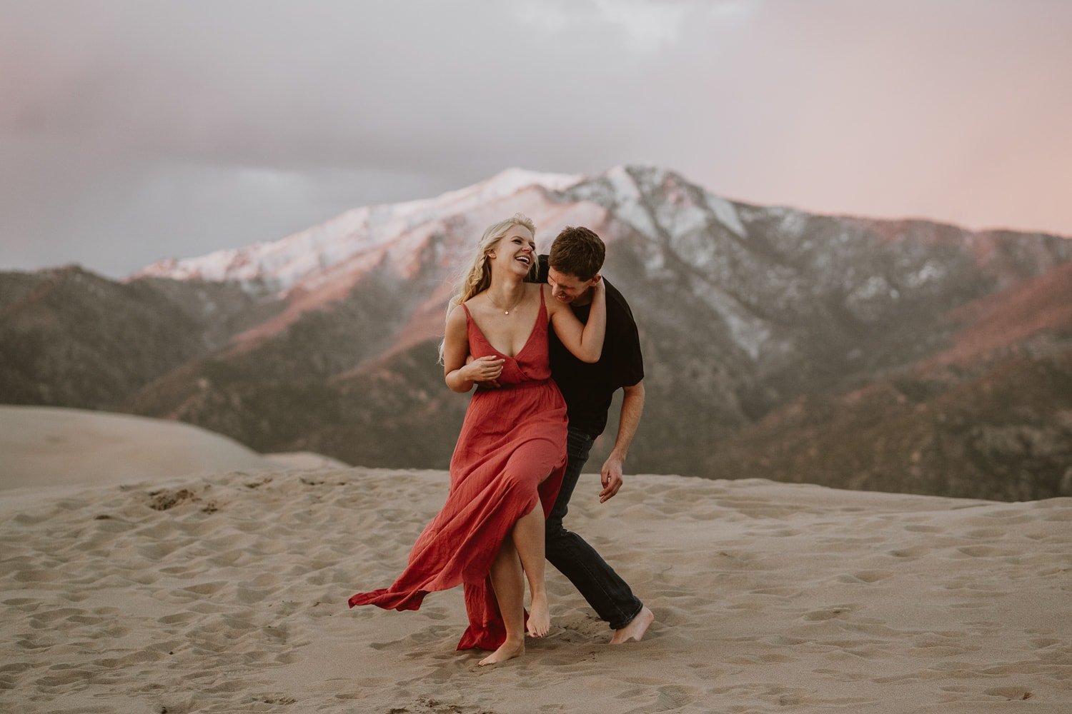 newly eloped couple laugh and dance at sunset on top of the great sand dunes in colorado