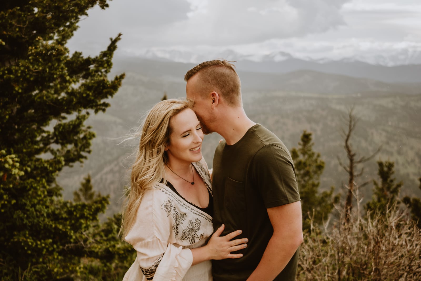 Adorable couple giggles and snuggle into each other during their moody mountain couples portrait shoot in Colorado