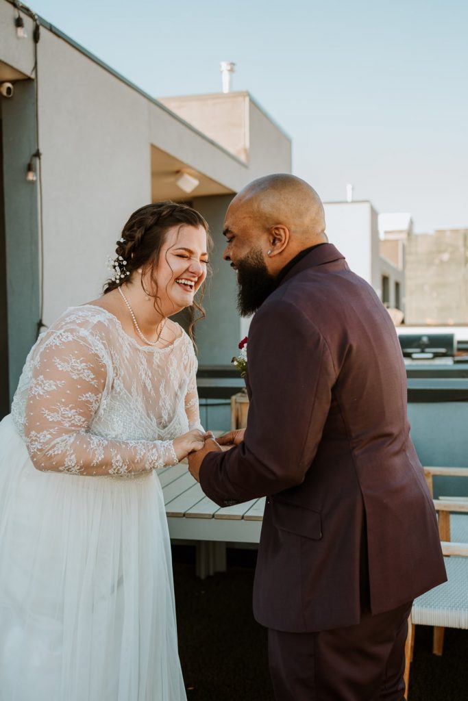 Couple standing on a rooftop patio laughing right after their first look.