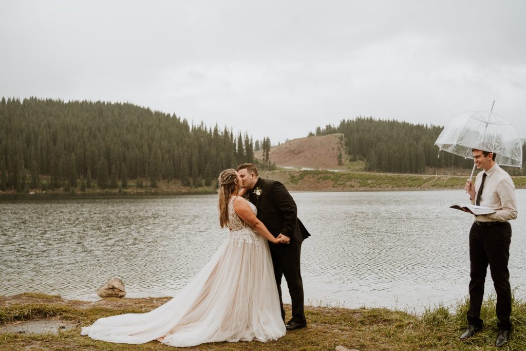 Bride and groom share their first kiss in the rain in front of a Colorado lake after they read their elopement vows.