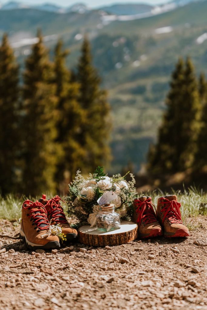 Matching pair of Danner mountain 600 hiking boots sits next to a bouquet. The Colorado mountains and pine trees are towering behind the shoes.