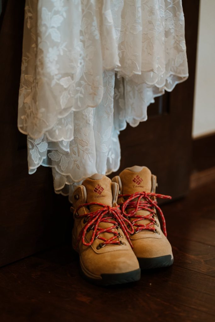 Brown pair of Columbia hiking boots with red laces and black soles sit beneath a lace white wedding dress.