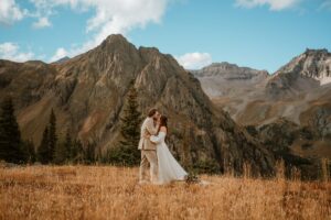 Bride and groom embrace each other for a first kiss. They are standing in a field surrounded by the mountains of Ouray Colorado.