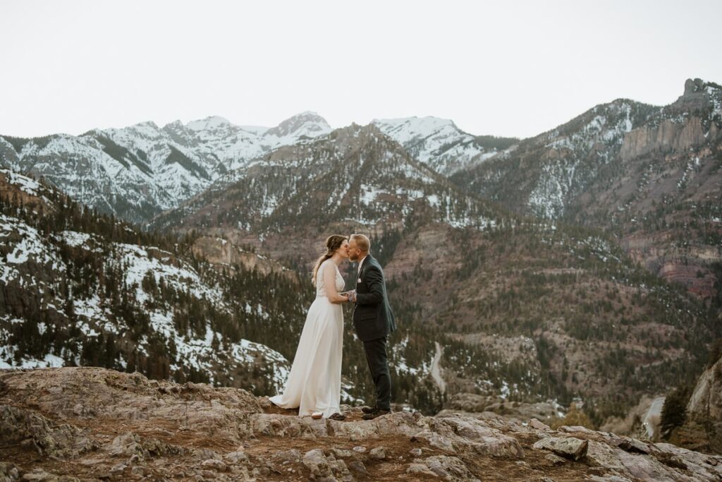 Bride and groom share a first kiss after eloping in Ouray Colorado. This couple eloped in April, so the mountains behind them still had snow on them.