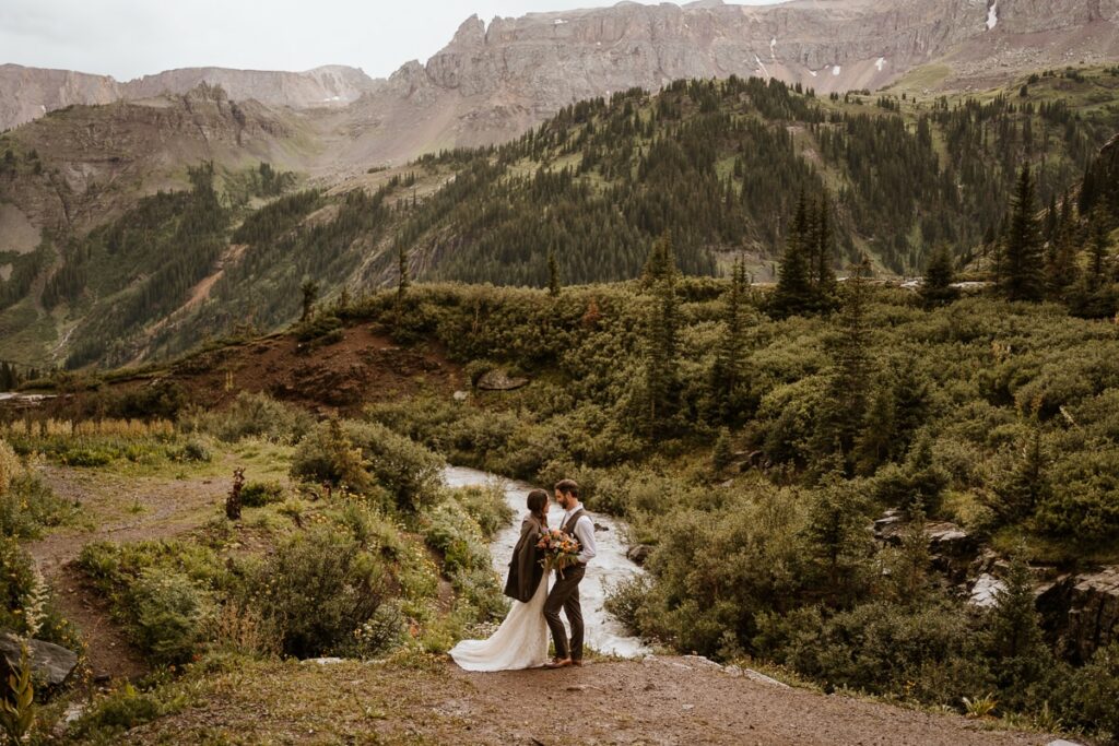 Newlywed couple stand in front of Twin Falls for a photo to show how big the mountains are in Ouray.