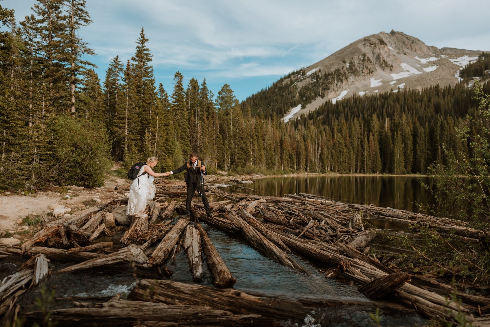The groom holds the brides hand and helps her across the log bridge that has to be crossed to make it to the final lake for their ceremony.