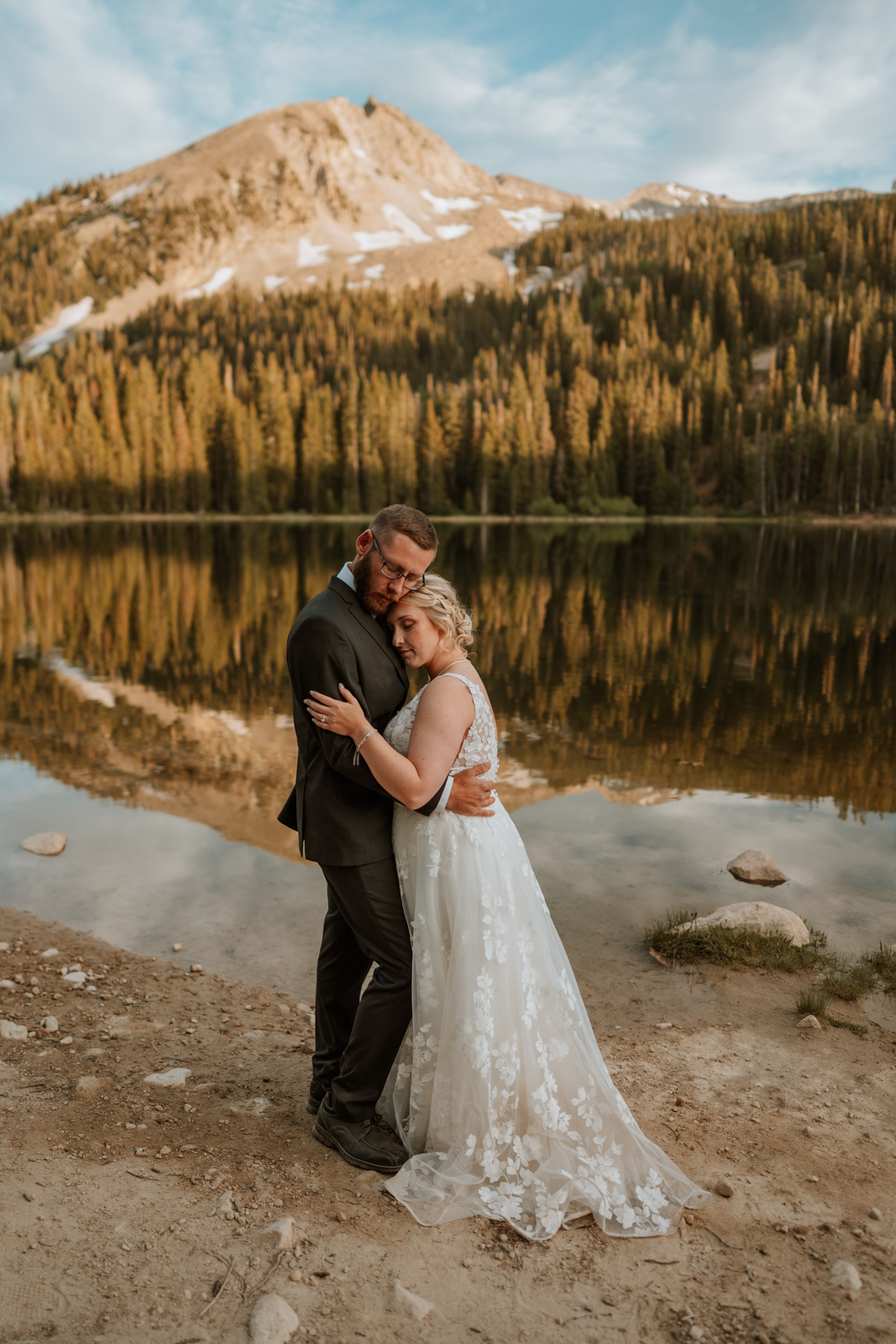 The bride and groom have a quiet moment in front of the reflective alpine lake in Crested Butte. They both close their eyes, hug each other close and take it all in.