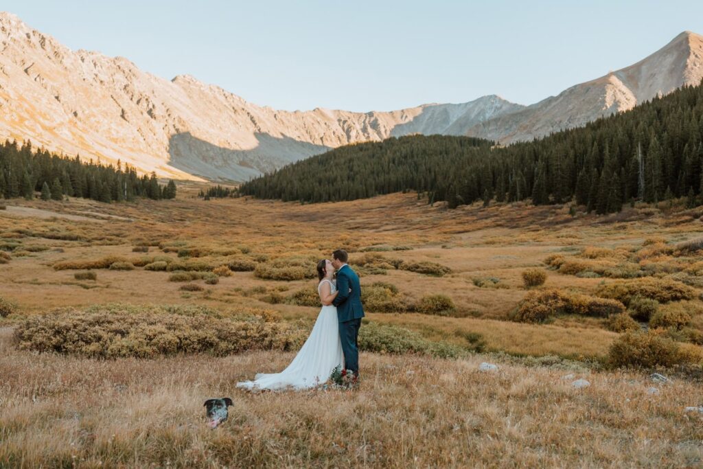 Newlyweds share another first kiss after their private vows at sunset near Breckenridge Colorado. The cut out of their dog's head is stuck in the ground near them.