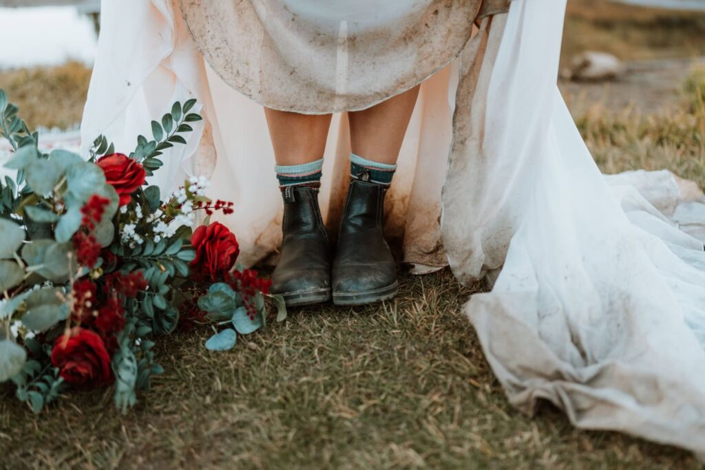 Closeup photo of a bride showing off her Blundstones with her wedding dress and bouquet.