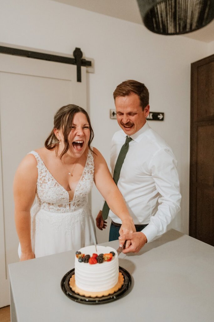 Bride laughs and has a huge smile on her face as she cuts the wedding cake with her new groom.