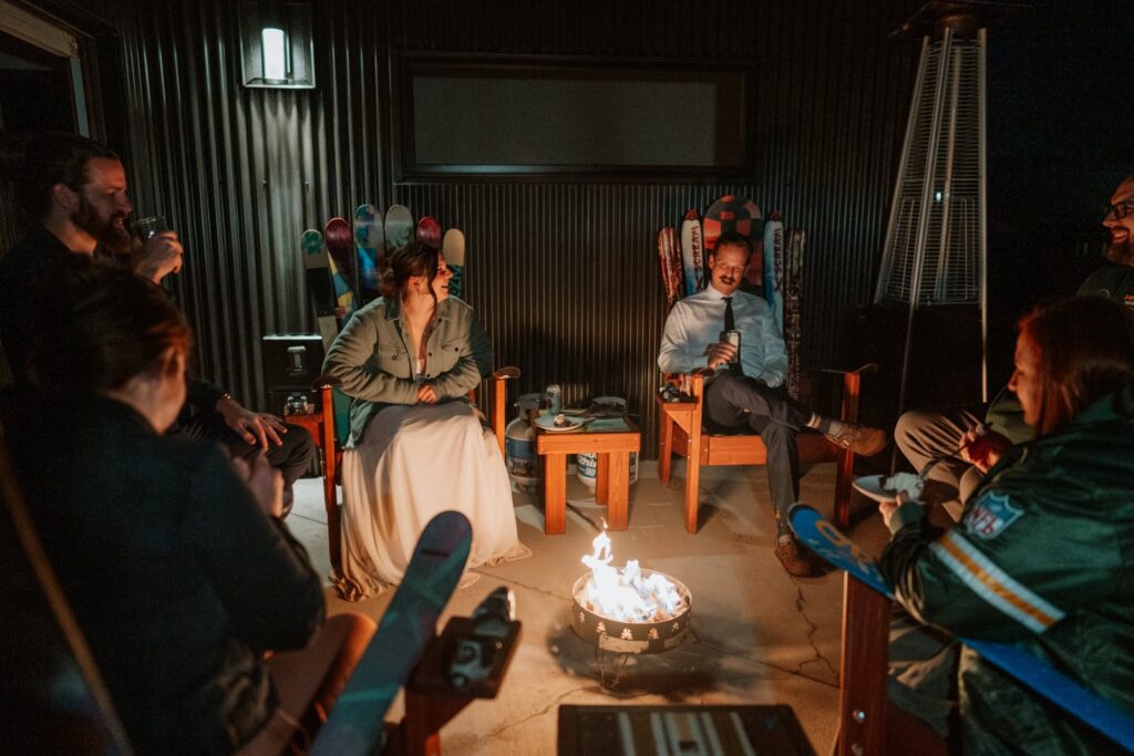 Wide photo that shows the bride and groom sitting by the propane campfire pit for their small mountain wedding in Colorado celebration.