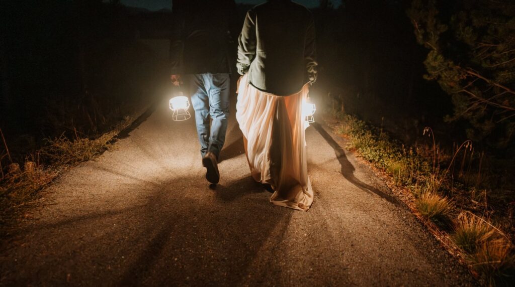 Closeup of bride and groom carrying 2 lanterns as they walk along a path in the dark.