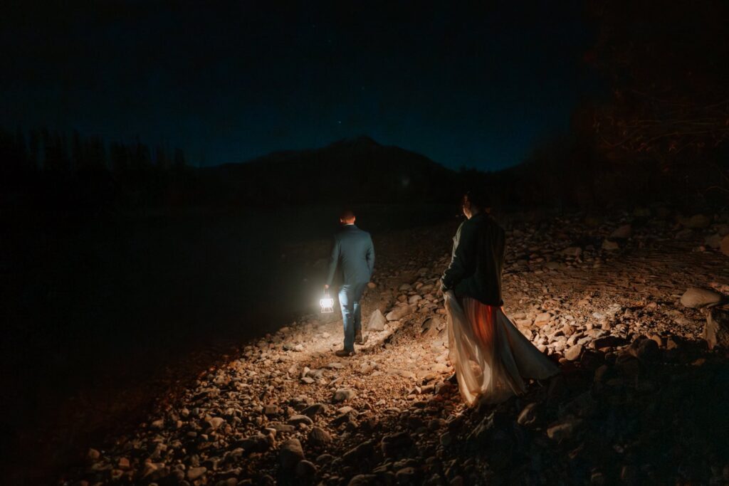 Bride and groom walk in the dark on a hiking trail near Dillon Reservoir by Breckenridge, Colorado. They are on their way to take star photos.