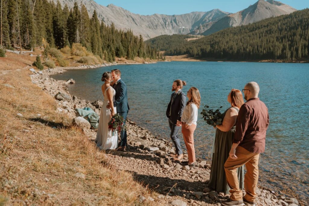 Bride and groom share a first kiss for their small mountain wedding in Breckenridge, Colorado with their 4 guests watching.