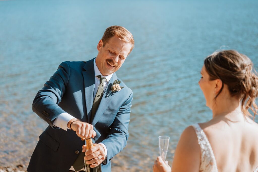 Groom pops open a bottle of champagne to celebrate with their guests at their small intimate wedding near Breckenridge.