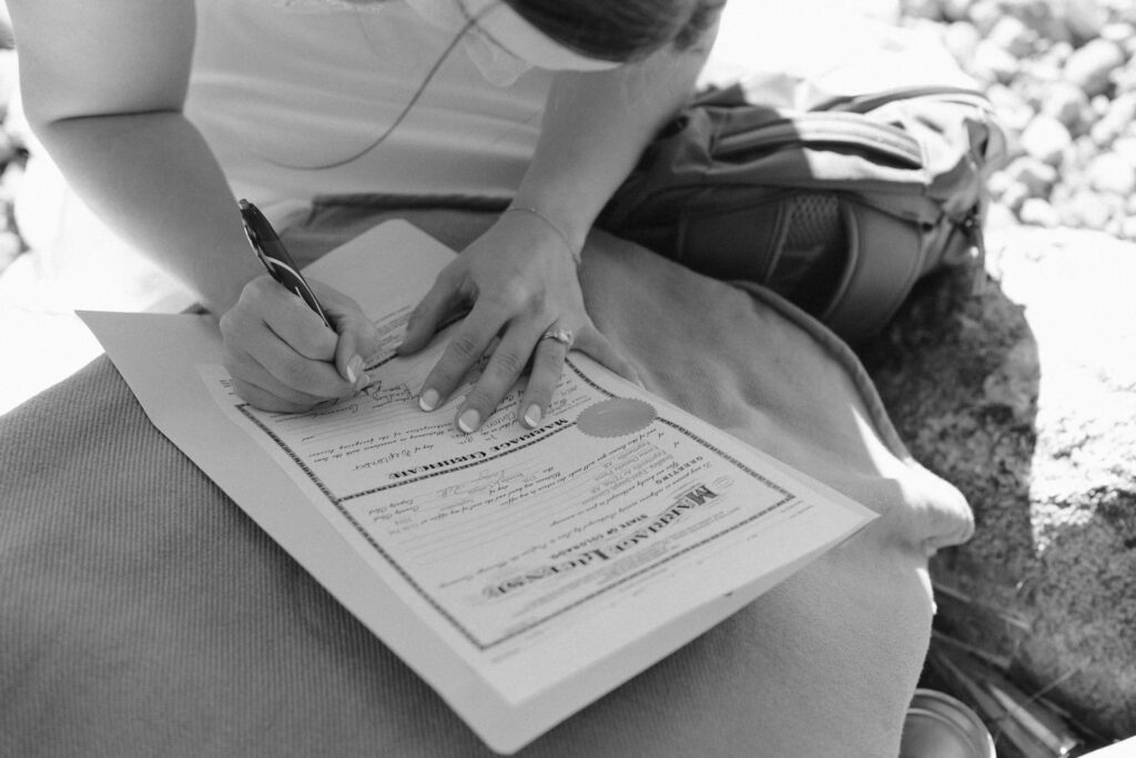Black and white photo showing the bride signing the marriage license for her Colorado elopement.