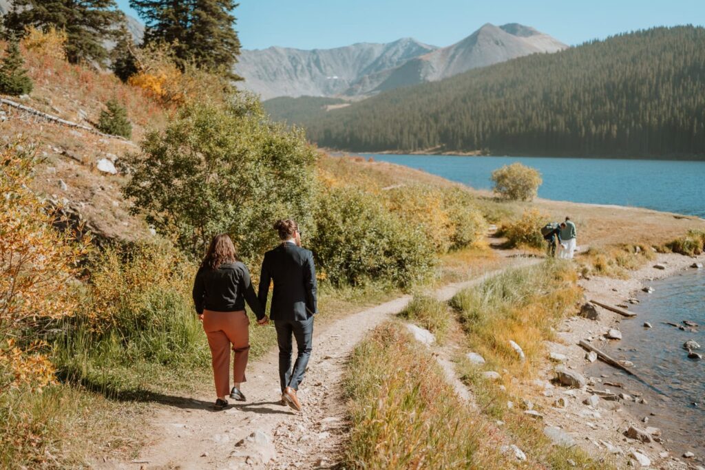 Two wedding guests walk down the hiking trail at Clinton Gulch reservoir in Breckenridge with the bride and groom not too far in front of them.