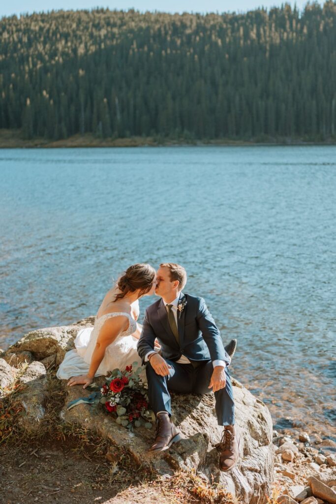 Bride and groom sit on a large rock next to Clinton Gulch reservoir in Colorado and share a kiss at sunset.