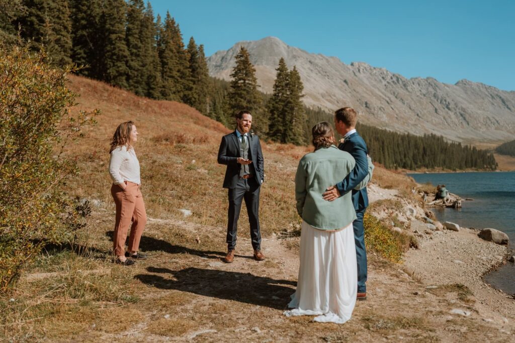 The best man reads a speech to the bride and groom from his cell phone. The mountains and trees stand tall behind all of them for this small wedding in Breckenridge.