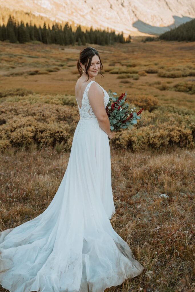 Bride poses for a solo portrait with her bridal train cast out behind her. The train has dirt on it from her adventures.