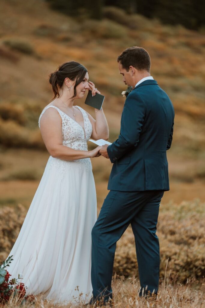 Bride wipes her tears away during emotional vow reading in the mountains of Colorado.