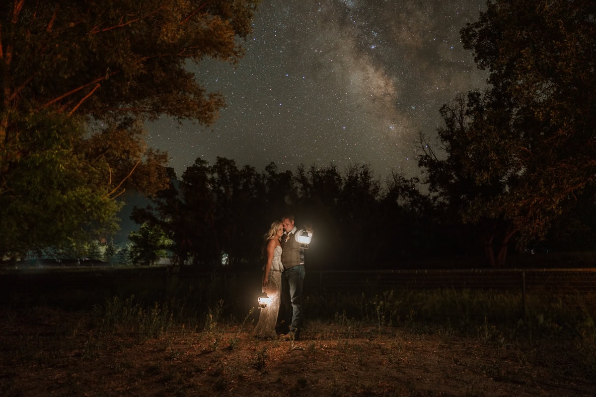 Couple pose for milky way photos while holding lanterns.