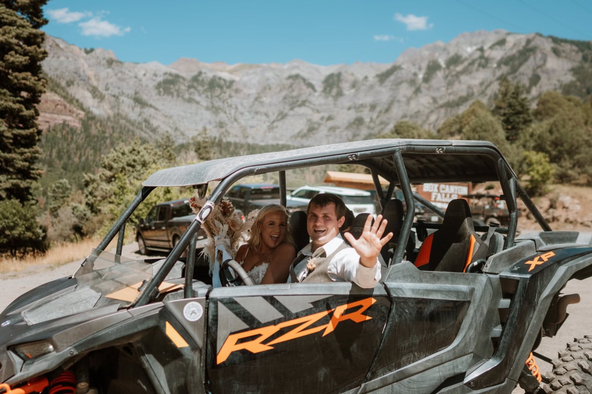 Bride and groom wave at the camera as they sit in their side by side for their Yankee boy basin elopement.