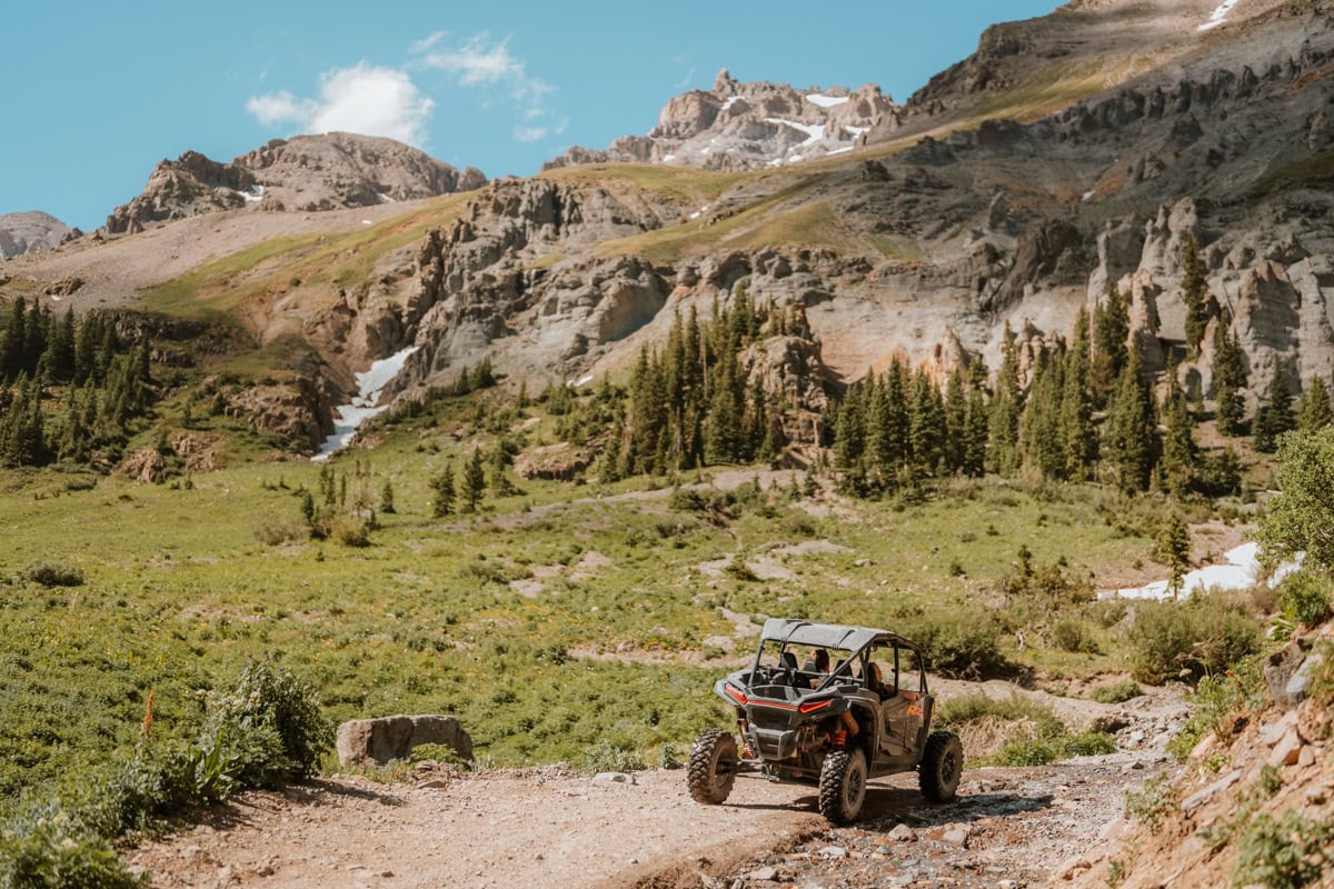 A side by side heads up the dirt road in Yankee boy basin with epic mountain views behind it.