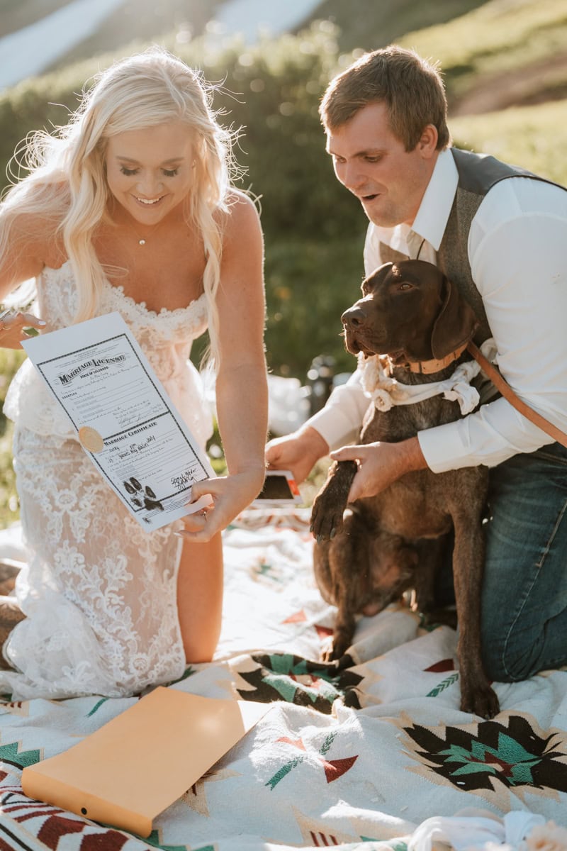Bride and groom smile and show off their dogs perfect paw print on their marriage license for their elopement in Yankee Boy Basin.