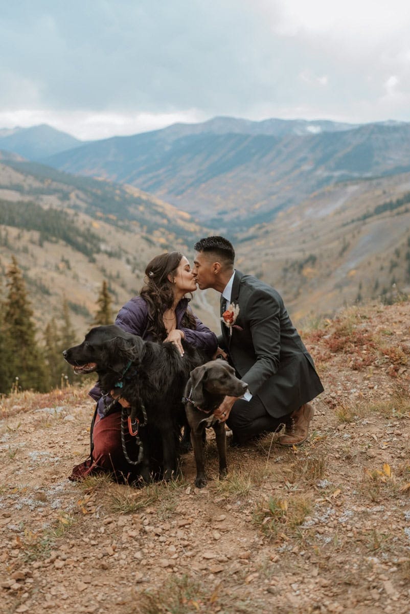 Couple sharing a kiss with their two dogs during a mountain elopement surrounded by fall colors.