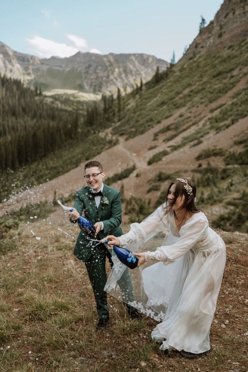 Joyful newlyweds popping champagne in the mountains to celebrate their adventurous elopement day and booking a Colorado elopement package that was true to them.