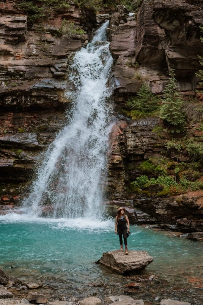 Paige Weber Photography, a Colorado elopement photographer, standing on a rock in front of a bright blue waterfall in Silverton, Colorado