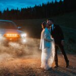 Couple sharing a kiss moment beside a 4x4 vehicle during a wedding in Telluride at night.