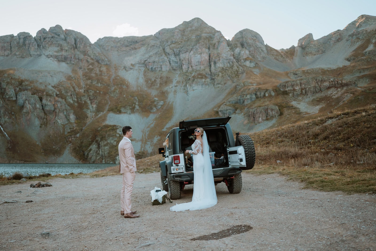 Bride in a wedding dress standing beside an open jeep with her partner in a mountain basin near Silverton during a jeep wedding.
