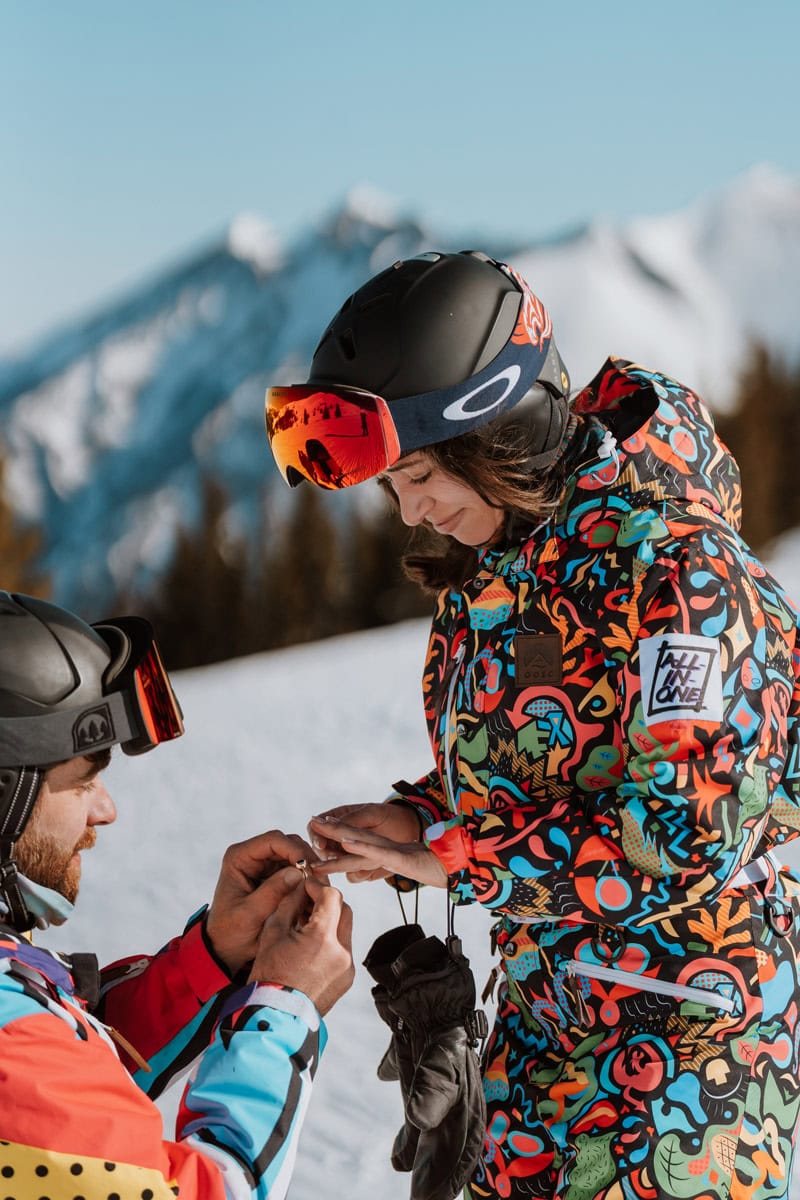 Close up of a groom-to-be putting a ring on his partner's finger during a winter ski proposal at Copper mountain ski resort.
