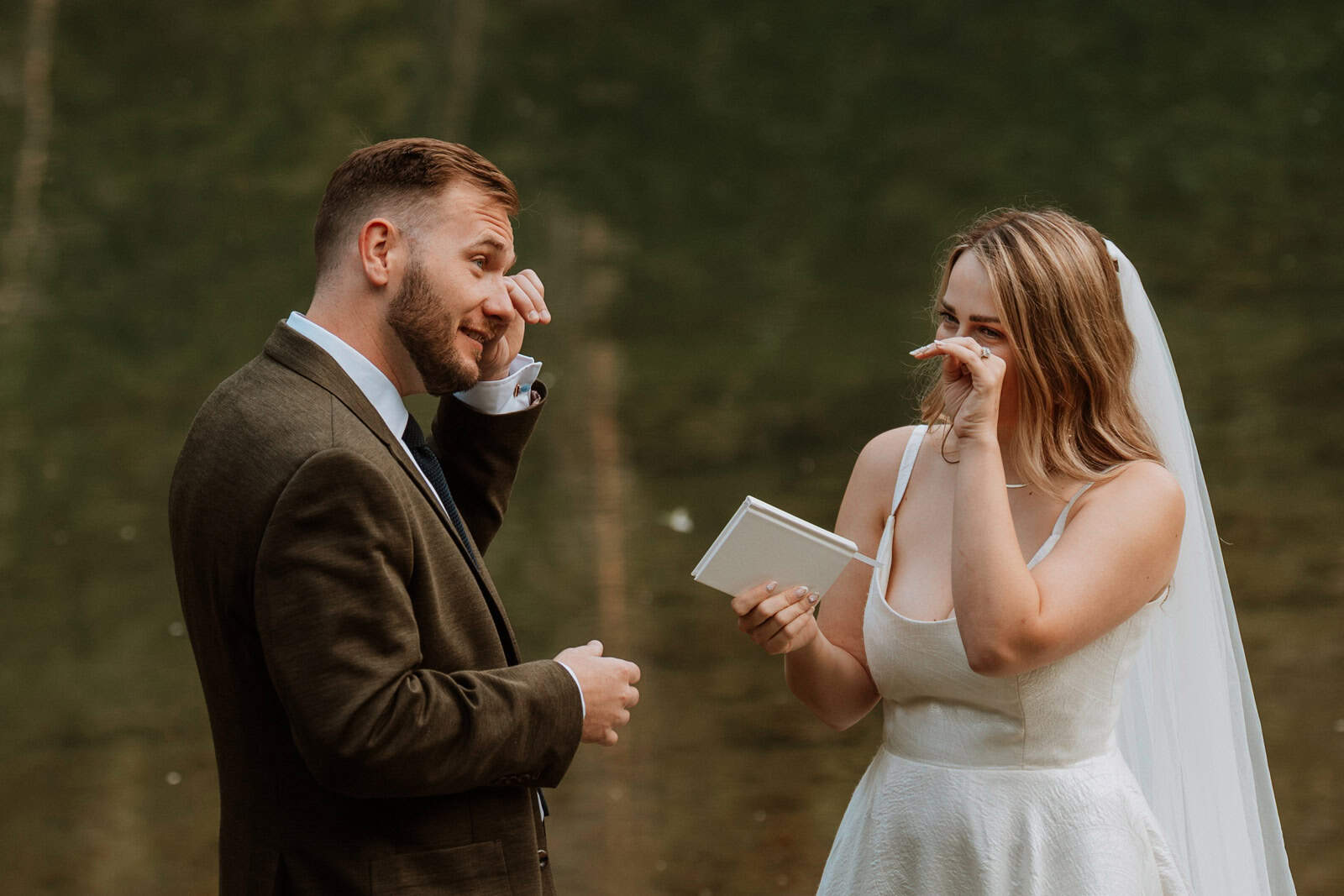 The bride and groom both wipe tears as she reads her vows during their emotional vow reading elopement.