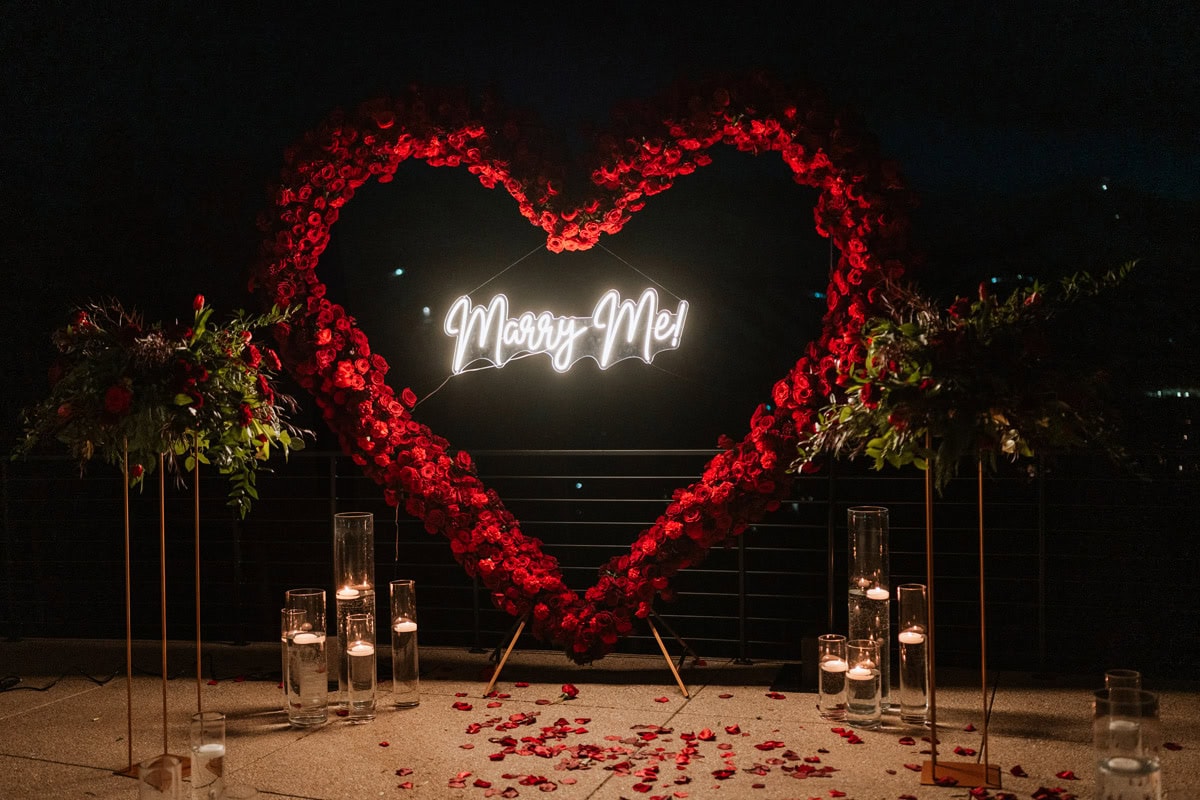 A heart-shaped red rose arch with a neon "Marry Me!" sign illuminated at night for an exclusive Colorado luxury proposal in Breckenridge.