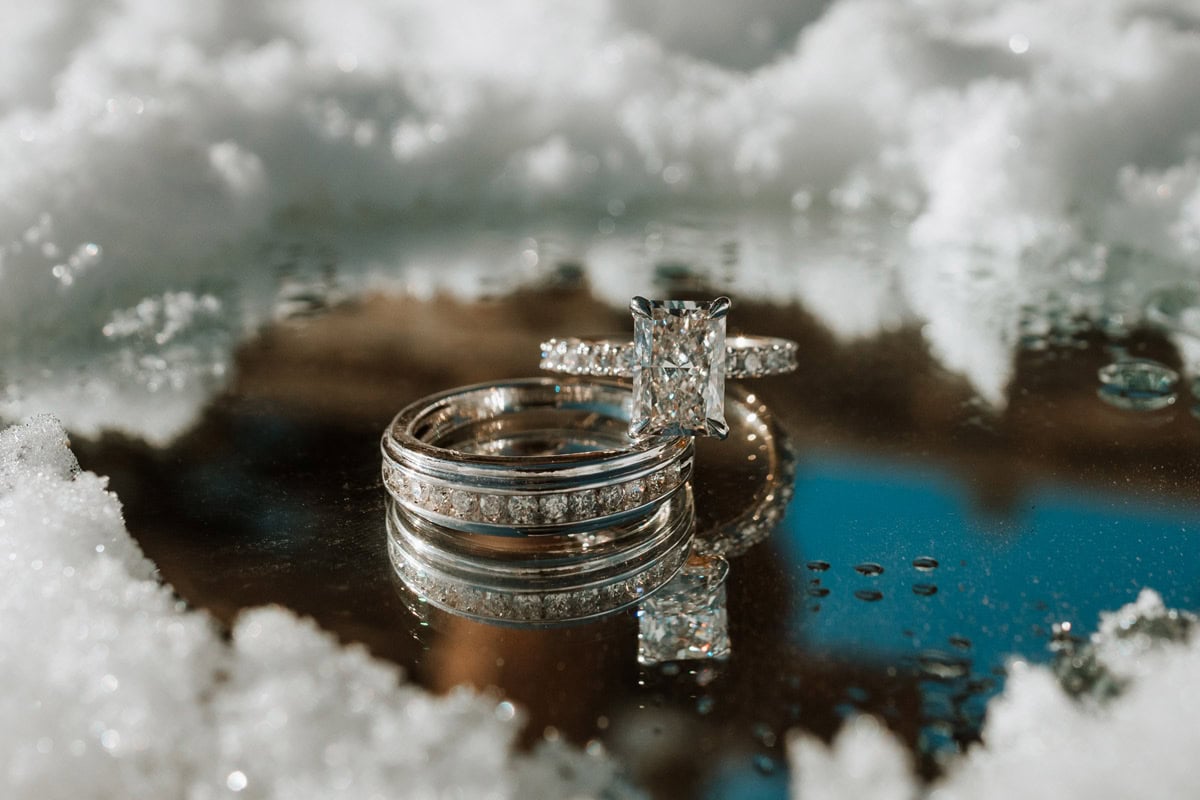 A close-up macro shot of a diamond engagement ring reflecting on a mirrored surface surrounded by fresh snow after a luxury proposal in Colorado.