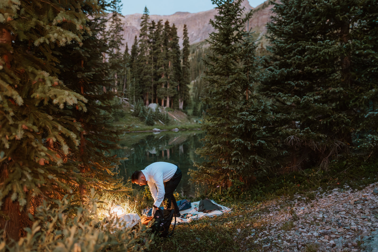 Groom sets up an area for the getting ready photos before sunrise beside a quiet alpine lake in the San Juan Mountains.