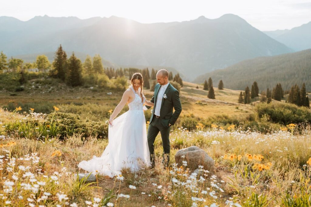 A bride and groom standing in a lush mountain meadow filled with white daisies during a sunrise elopement in the San Juan Mountains.