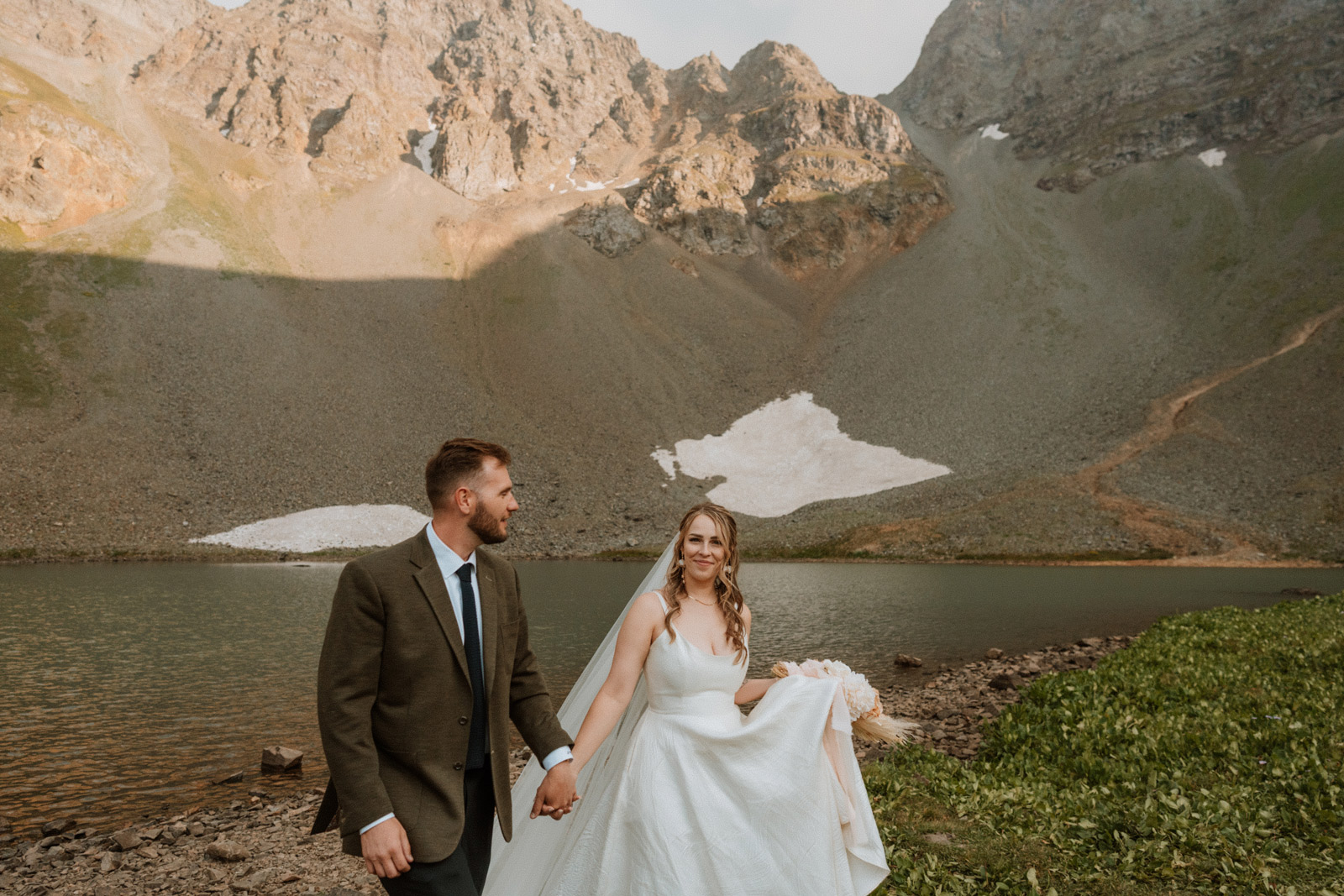 Bride and groom walk together beside an alpine lake during golden hour in the backcountry near Silverton at their sunset elopement.