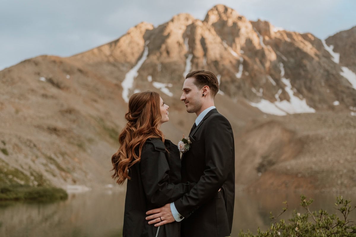A romantic portrait of an elopement couple looking at each other as the golden hour light hits the rocky peaks behind them.