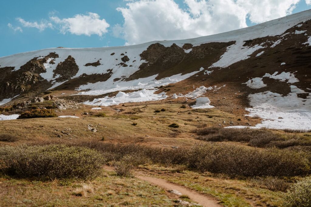 A sweeping landscape view of a dirt trail leading up toward beautiful snow-covered mountain peaks.
