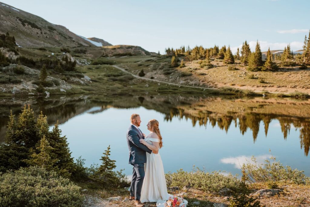 A couple embraces on the shore with the landscape perfectly mirrored in the water behind them, highlighting the scenic beauty of their Loveland Pass elopement.